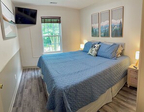 A bedroom with a bed, a TV mounted on the wall, a window with blinds, and artwork on the wall. - Reid Cottage |3Bd/2Bth Ranch |King Beds |Sleeps 8 (Charlotte)