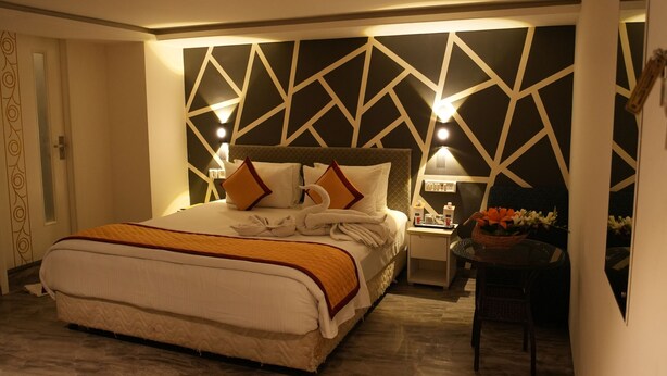 A well-lit bedroom with a large bed, a nightstand, and a small table with a lamp. - Citrus Classic Mambakkam Chennai (Tirupporur)