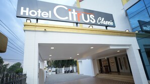 The entrance of Hotel Citrus Classic with a clear sign above the entrance, a tiled walkway leading inside, and a visible outdoor area with a fence and parked motorcycles.