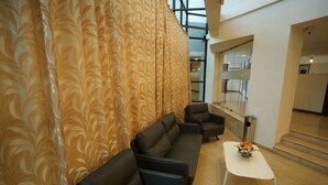 A modern interior with a black leather sofa, a white table with a flower arrangement, and patterned curtains.