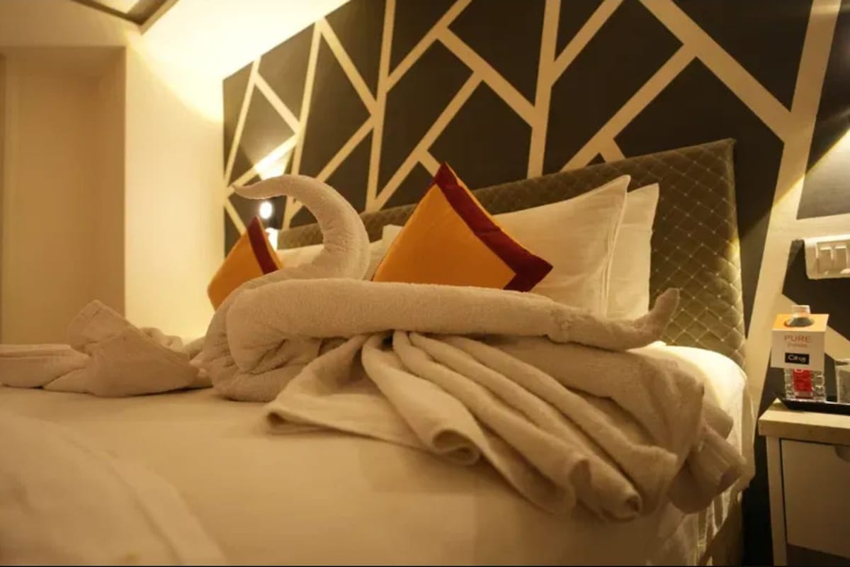 A hotel room with a neatly made bed, a bedside table with a bottle, and a geometric-patterned headboard.
