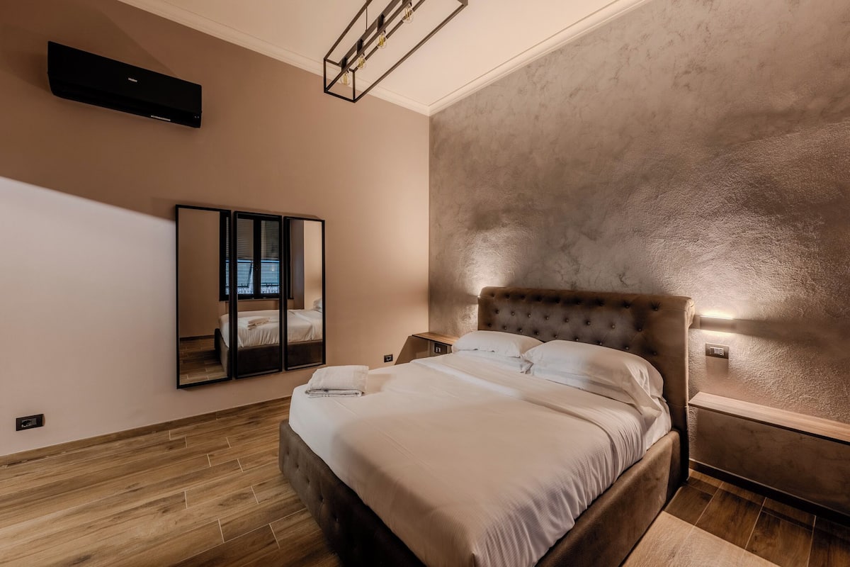 A bedroom with a bed, a nightstand, a mirror, and a wall-mounted air conditioner.