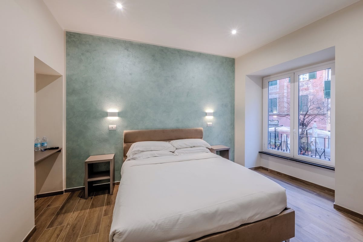 A bedroom with a bed, bedside tables, a nightstand, a window with a view, and a wall with a textured finish.