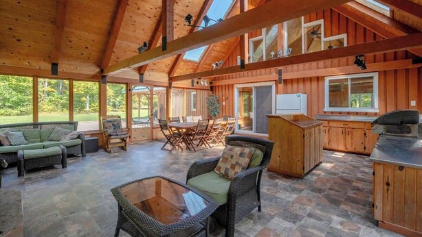Un vaste espace intérieur doté de hauts plafonds et de poutres en bois, comprenant un coin repas avec des chaises et une table, un canapé et un coin cuisine avec un comptoir et des placards.