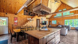 Un intérieur de chalet en bois spacieux, doté d’un îlot central, d’un coin repas et d’un espace de vie confortable avec un canapé et un téléviseur.