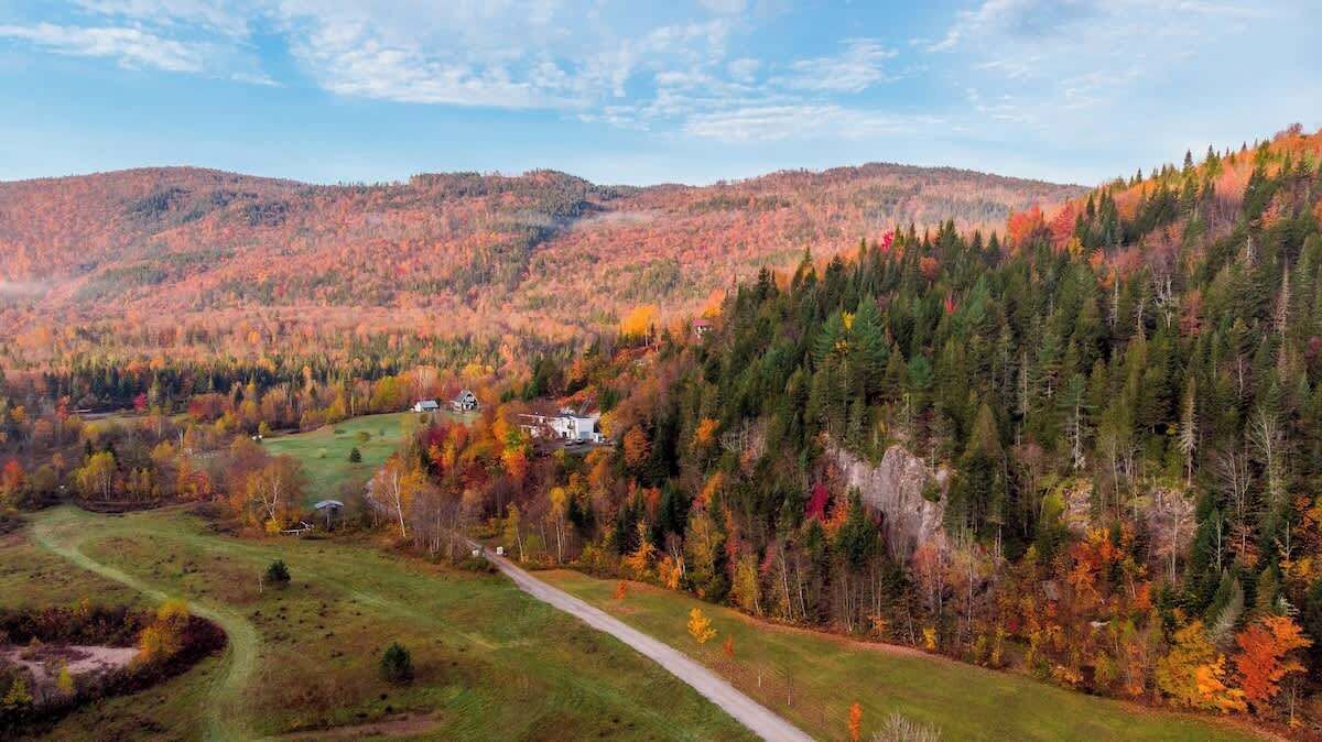 Paisagem rural com estrada sinuosa, uma casa pequena e colinas arborizadas.