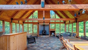 Un chalet spacieux avec un haut plafond en bois, un plancher en pierre et de grandes fenêtres offrant une vue sur la forêt.