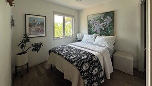 A bedroom with a bed, a window, a painting, and a radiator.