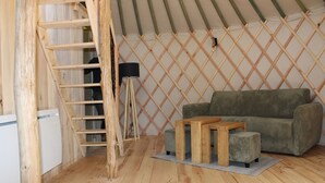 A room with a wooden ladder, a sofa, a small table, and a lamp against a lattice wall. - Yurt rental 2 / 4 / 6 persons (Saint-Amans-des-Cots)