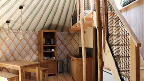 A wooden interior with a dining table, benches, a bookshelf, and a staircase with a net barrier. - Yurt rental 2 / 4 / 6 persons (Saint-Amans-des-Cots)