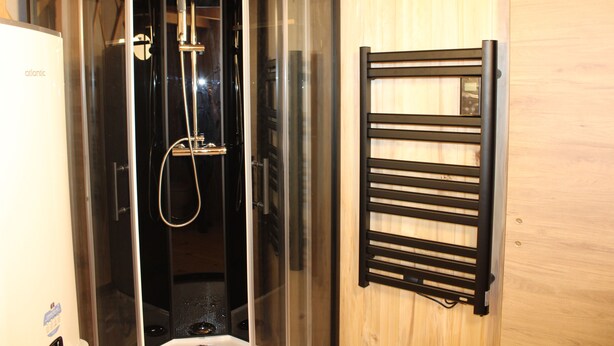 Ein modernes Badezimmer mit einer gläsernen Duschkabine, einem schwarzen Handtuchhalter und einer Holzvertäfelung.