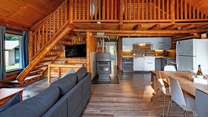 A log cabin interior with a wooden staircase, a living area with a sofa, a dining table, and a kitchen with modern appliances.