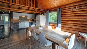 A modern log cabin interior with a dining area, kitchen, and a staircase leading to an upper level.