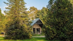 A cabin surrounded by dense forest, with a clear path leading to the entrance.