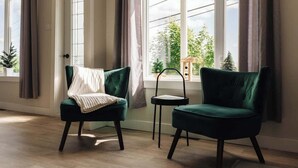 Een kamer met twee donkergroene stoelen, een tafeltje en uitzicht op groen buiten door grote ramen.