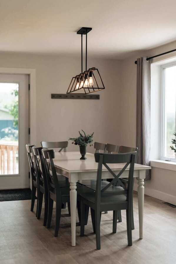 Un comedor con una mesa rectangular, seis sillas, una lámpara colgante y una planta en maceta.