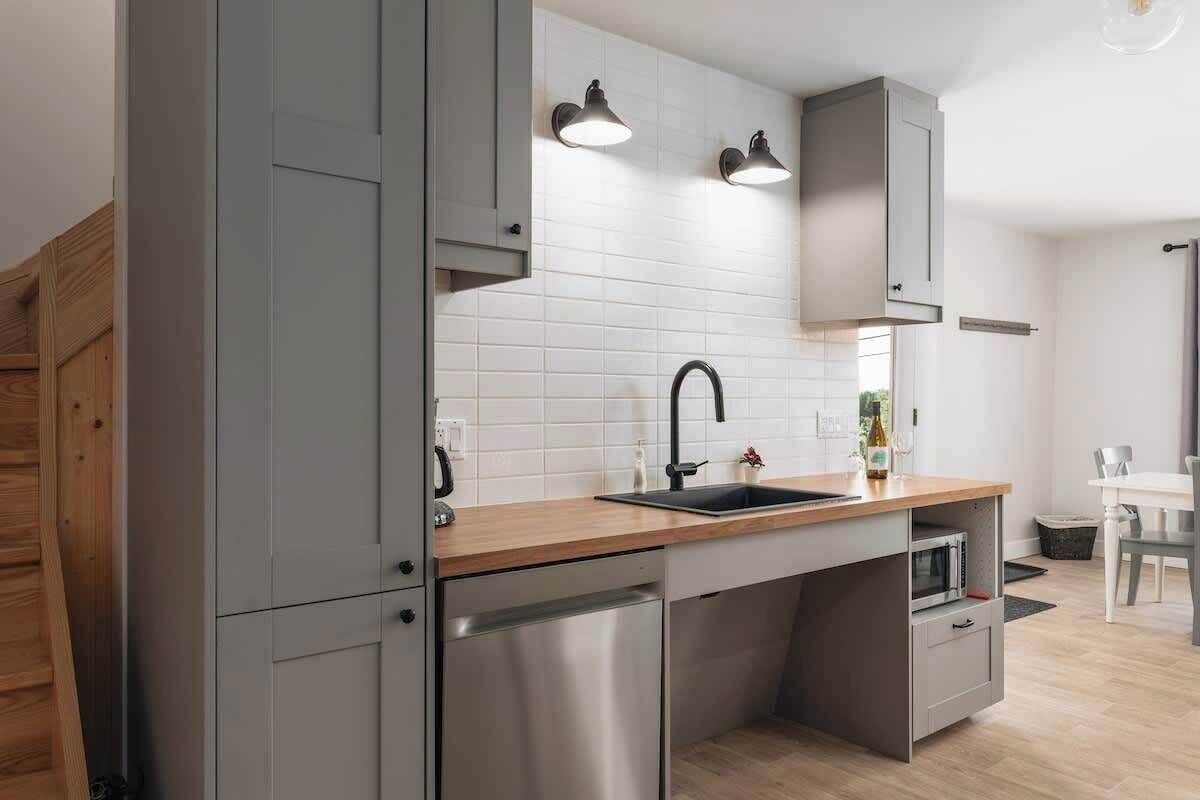 A modern kitchen with grey cabinets, a wooden countertop, a stainless steel dishwasher, and a built-in microwave.
