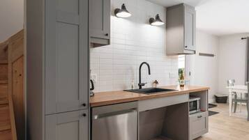 A modern kitchen with grey cabinets, a wooden countertop, a stainless steel dishwasher, and a built-in microwave.