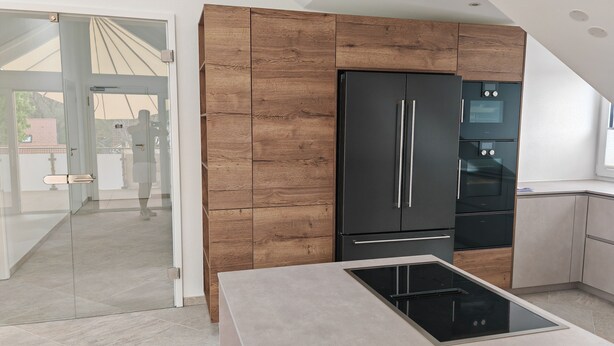 A modern kitchen with a built-in oven, a large black refrigerator, and a glass door leading to an outdoor area. - Ultra-modern penthouse apartment (Brunnthal)