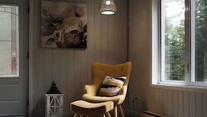 Une pièce dotée d’une grande fenêtre, d’un fauteuil avec un coussin, d’une œuvre d’art accrochée au mur et d’un luminaire suspendu.