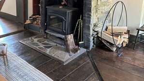 Un interior rústico con chimenea de piedra, piso de madera y una escalera que lleva a otra habitación.
