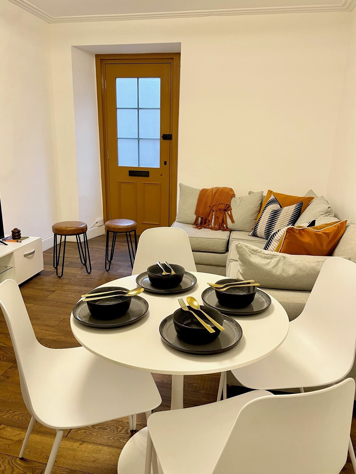 A dining area with a round table set for four, white chairs, and a sofa with cushions.