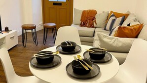 Un comedor con una mesa redonda dispuesta para cuatro personas, sillas blancas y un sofá con cojines.