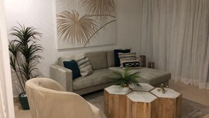 Una sala de estar con un sofá color crema, una mesa redonda de madera y un cuadro abstracto grande en la pared.