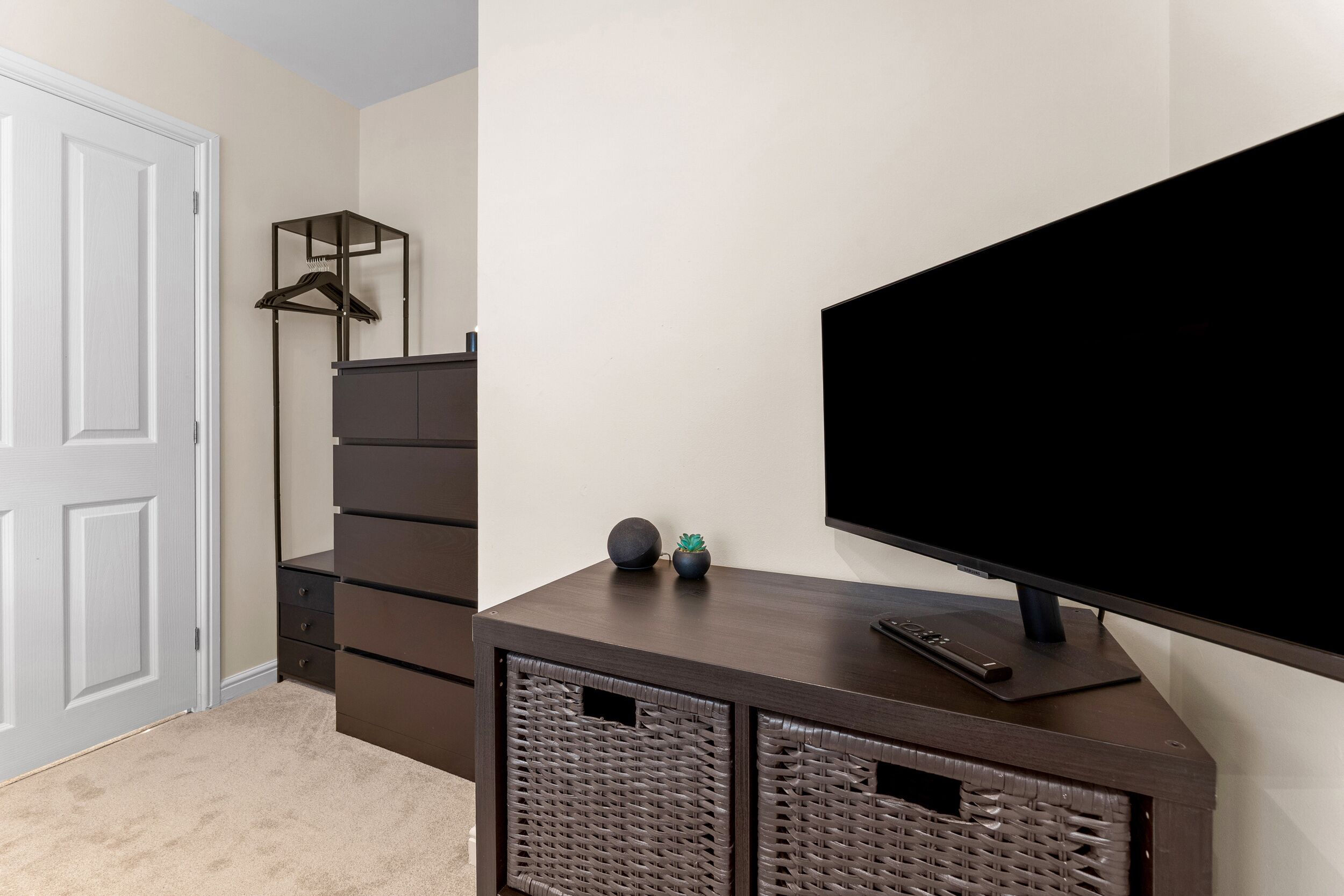 A room with a dark wooden TV stand, a flat-screen TV, a white door, and a wall-mounted coat rack.