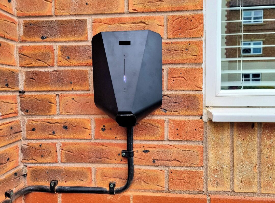 A black outdoor unit mounted on a brick wall, connected to a window with a white frame.
