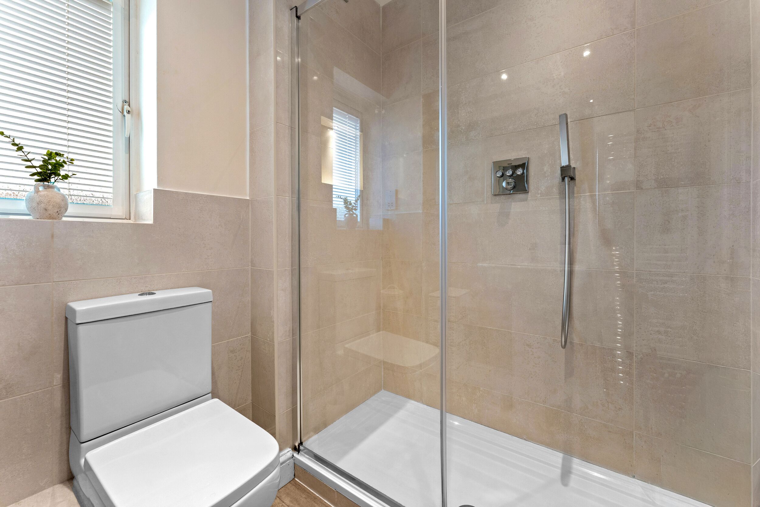 A modern bathroom with a glass-enclosed shower, a toilet, and a window with blinds.