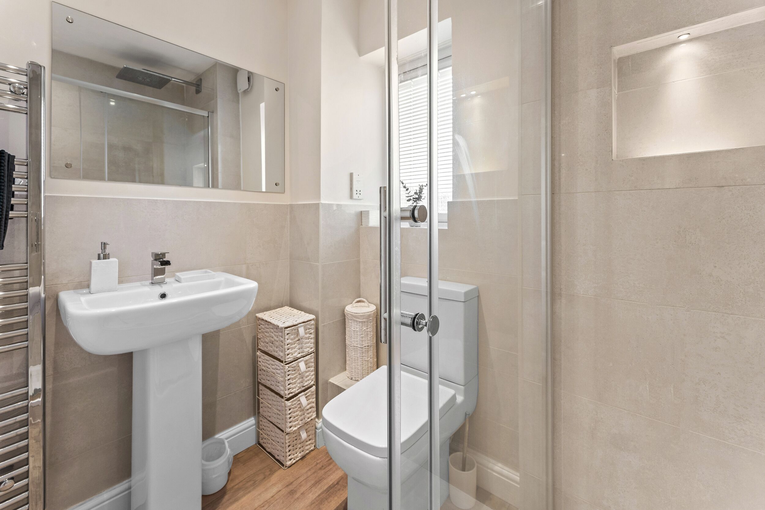 Un baño moderno con un lavamanos pedestal blanco, cabina de ducha con mampara de vidrio y un inodoro con tanque blanco.