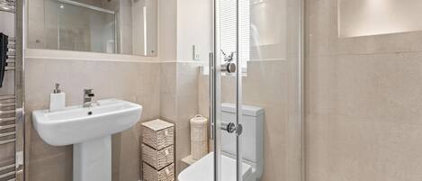 Un baño moderno con un lavamanos pedestal blanco, cabina de ducha con mampara de vidrio y un inodoro con tanque blanco.