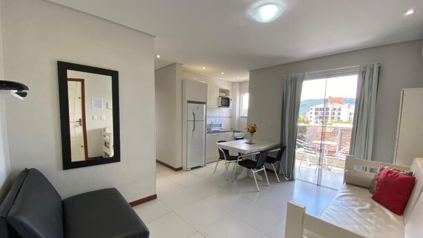 A modern hotel room with a balcony, a dining area, and a kitchenette. - Beautiful 1 bedroom apartment with balcony and barbecue 70m from Praia dos Ingleses (Ingleses Sul Florianópolis)