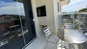 A balcony with a glass door, a metal table, and chairs. - Beautiful 1 bedroom apartment with balcony and barbecue 70m from Praia dos Ingleses (Ingleses Sul Florianópolis)