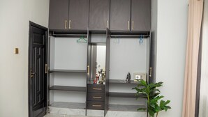 A room with a dark-colored wardrobe featuring multiple shelves and drawers, a small plant, and a door.