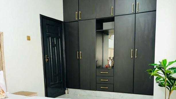 A bedroom with a bed, a large wardrobe, and a potted plant.