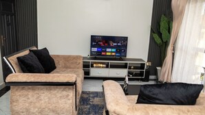 A modern living room with a flat-screen TV mounted on the wall, a beige sofa, and a matching armchair.