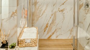 A modern bathroom with marble walls, a glass shower enclosure, and a wooden floor. - Ayla Studio Athens (Imittos)