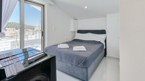 A modern hotel room with a large bed, a desk with a computer, and a sliding glass door to the outside. - Ayla Studio Athens (Imittos)