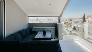 A balcony with a dark-colored sofa, a small table with a potted plant, and a city view. - Ayla Studio Athens (Imittos)