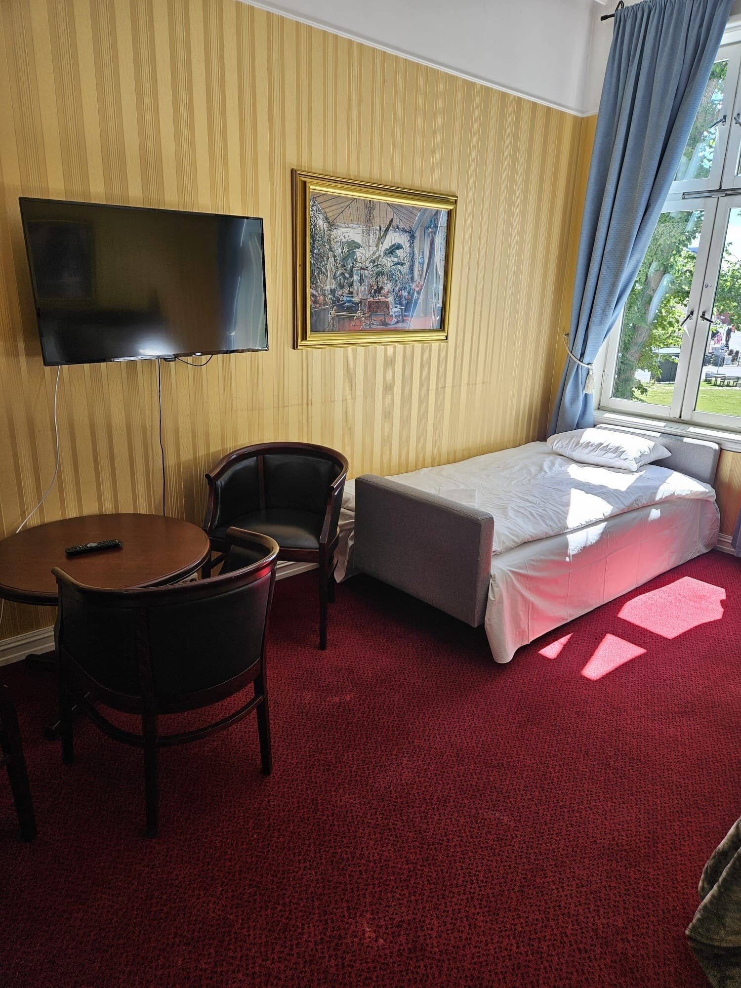 Habitación de hotel con cama, televisión, silla, mesita y ventana con cortinas.