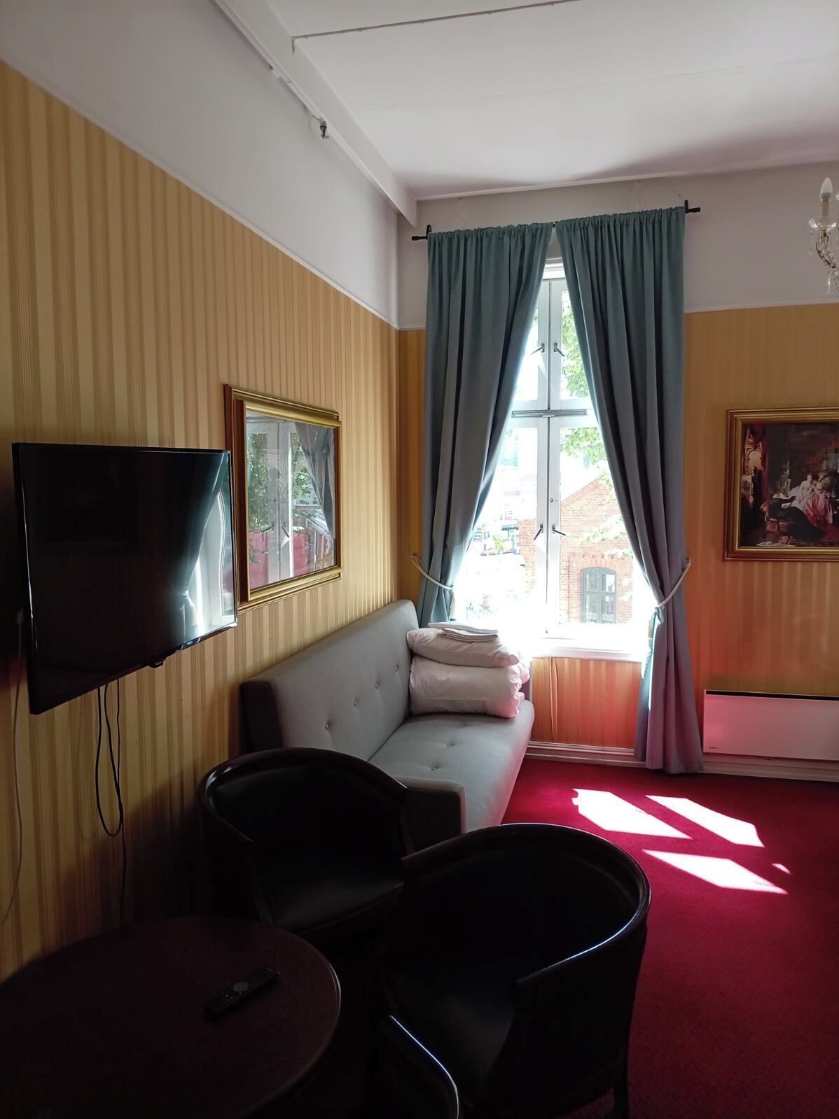 A room with a sofa, a TV mounted on the wall, a window with curtains, and a painting on the wall.