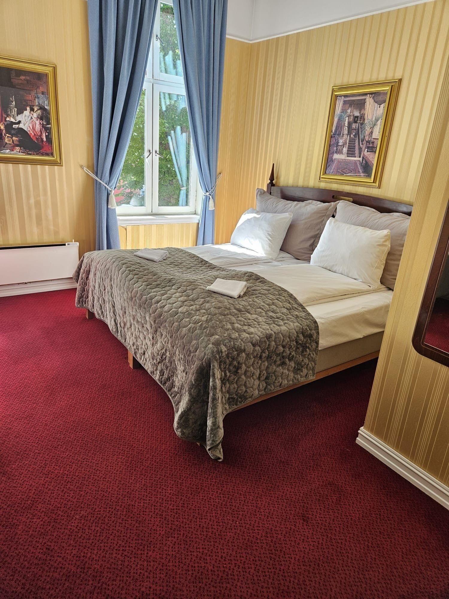 Un cuarto de hotel con una cama grande, una ventana con cortinas y dos cuadros en las paredes.