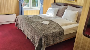 A hotel room with a large bed, a window with curtains, and two framed pictures on the walls.