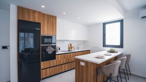A modern kitchen with wooden cabinets, a built-in oven, a sink, and a large island with bar stools.