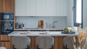 A modern kitchen with white cabinets, a Bosch oven, a coffee maker, and a dining area with three chairs.