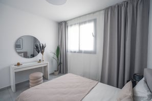 A modern bedroom with a bed, a bedside table, a mirror, and a window with curtains. - Mira Paphos - 2bdr Apartment With Private Terrace (Paphos)
