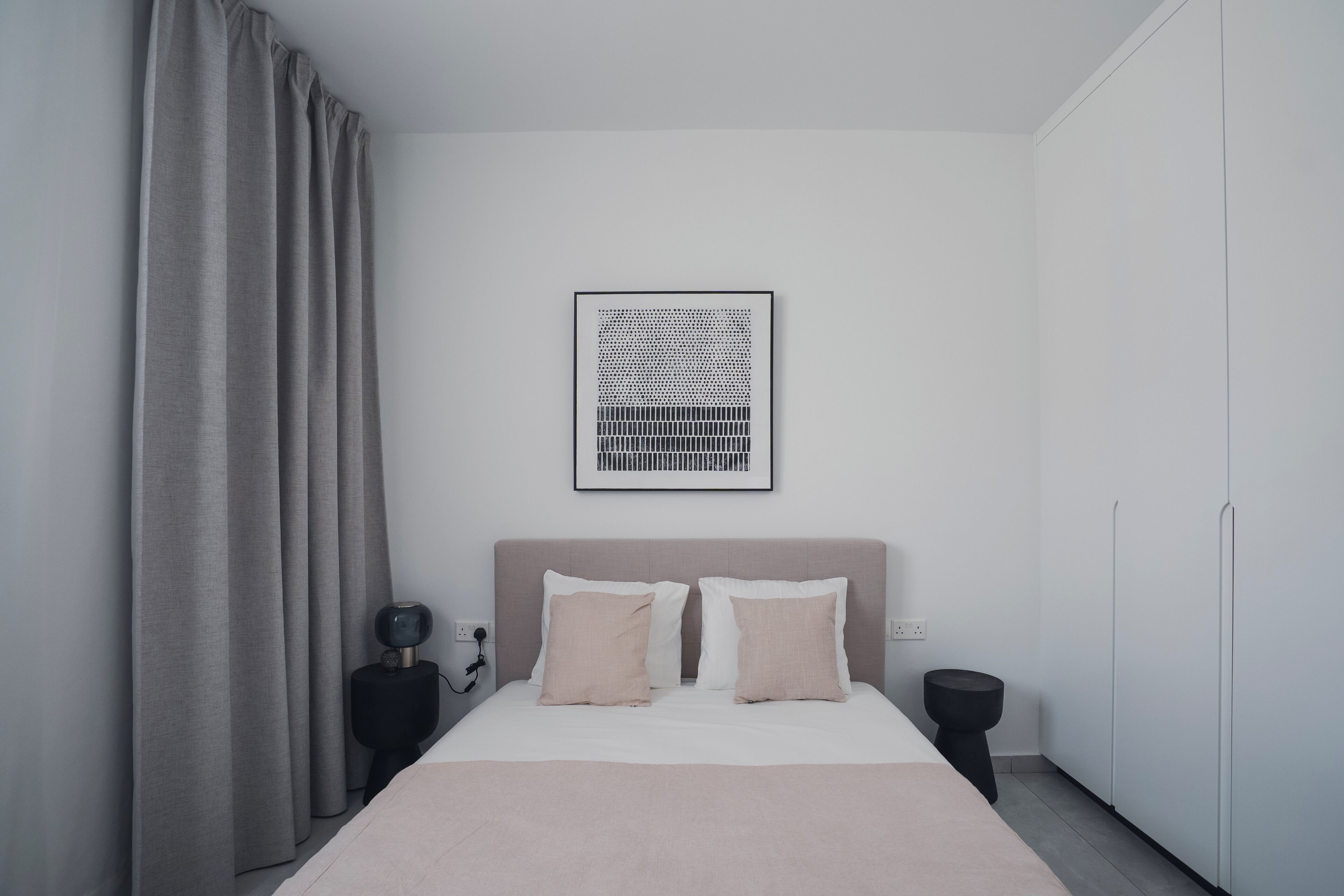 A minimalist bedroom with a bed, two bedside tables, a wall-mounted picture, and a wardrobe.
