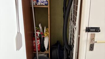 Un lavadero pequeño equipado con lavadora, aspiradora y productos de limpieza.